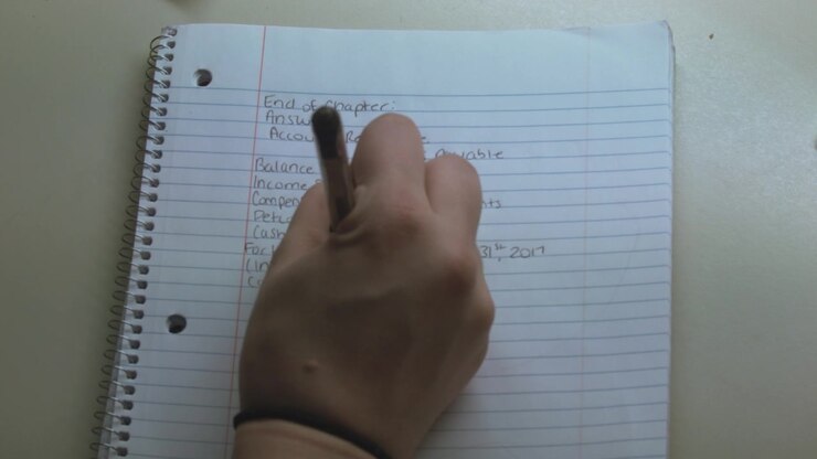 A close-up of a caucasian hand writing down notes during an economy class.