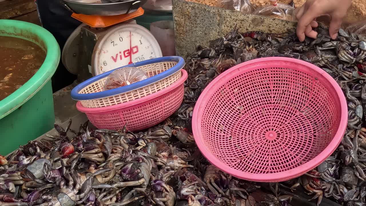 A vendor sorts crabs using pink and blue baskets at a market stall.