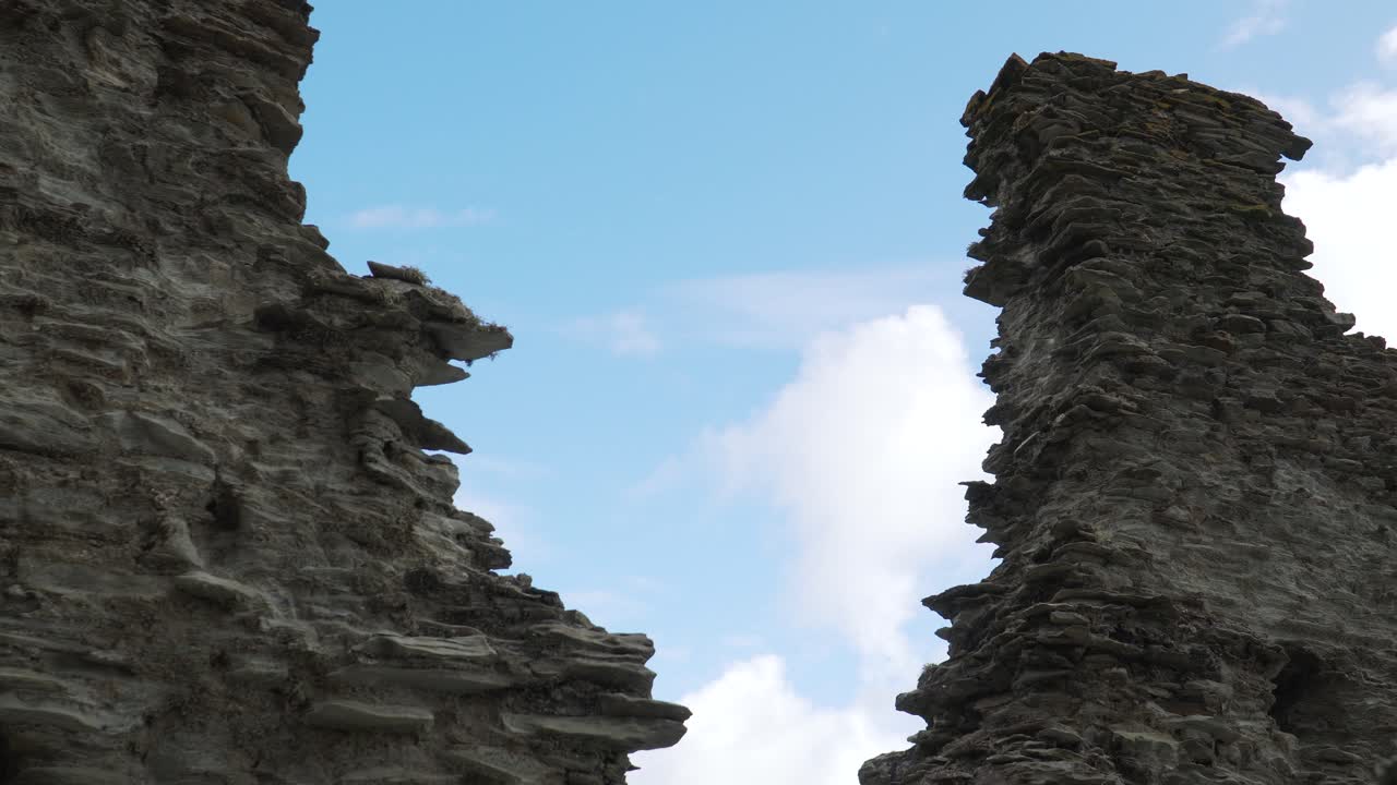 Close up view of one of the Tintagel Castle is a medieval fortification located on the peninsula of Tintagel, Cornwall . Medieval fortification in U shape, blue sky and some clouds in the background