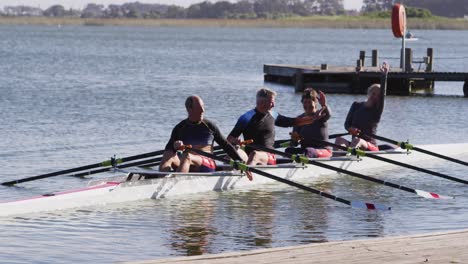 four senior caucasian men and women in rowing boat raising hands and cheering