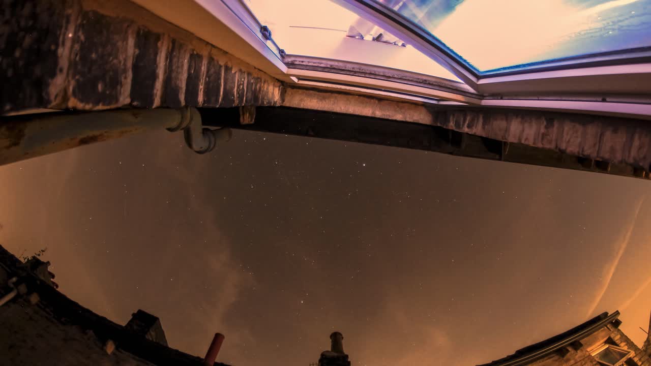 el cielo nocturno pasa mientras la gente vive sus vidas viendo la televisión en el interior