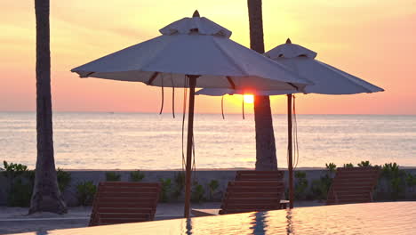 a bright pink, red and orange tropical sunset peeks out from under two beach umbrellas