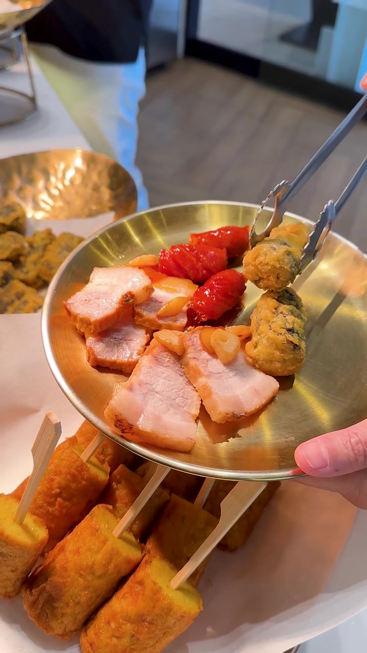 Primer plano de manos usando pinzas para servir empanadillas fritas y panceta de cerdo en un plato