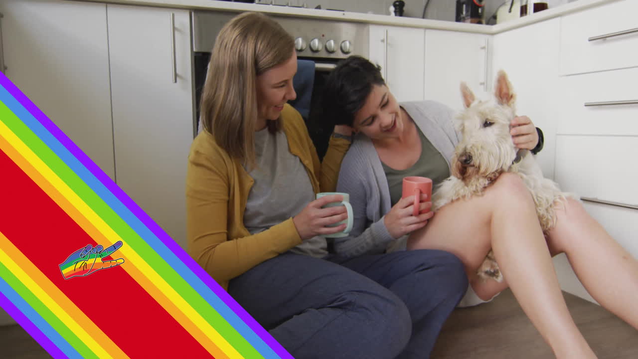 Animation of pride rainbow stripes and hand over caucasian lesbian couple in kitchen with pet dog