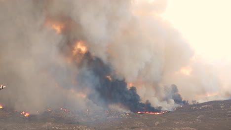 huge wild fire rages, tall columns of black smoke rise