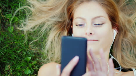 Attractive-Young-Woman-Lies-On-Grass-Enjoys-Smartphone-Hair-Beautifully-Lie-On-The-Lawn-4k-Slow-Moti