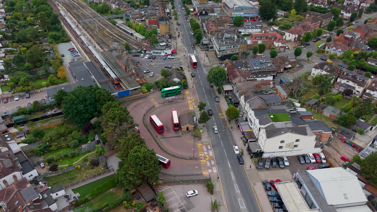 Smooth drone orbit of Chingford Bus Terminal and Train Station in East London, featuring red and green double-decker buses and train in the station