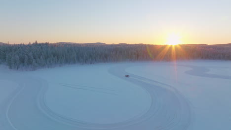 driver drifting corners on lapland ice lake race track as sunrise rises from woodland aerial view