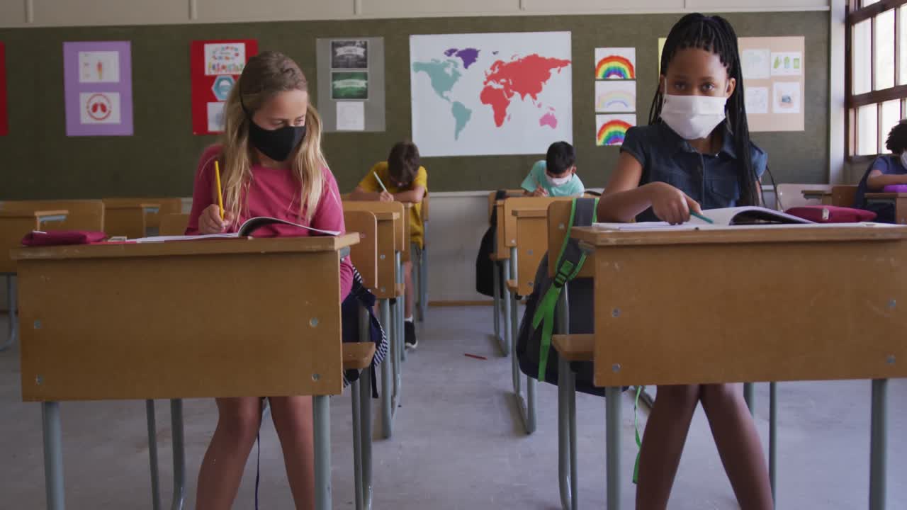 dos niñas con máscaras faciales saludándose las unas a las otras tocándose los codos en la escuela
