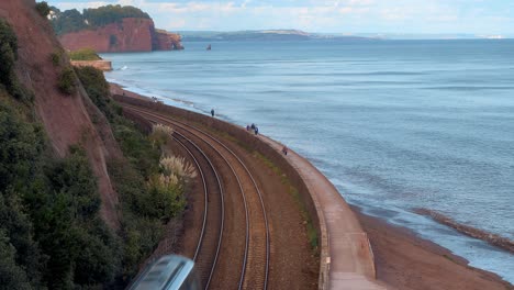 gwr class 800 penzance to paddington train passes slowly along the stunning south devon sea front between teignmouth and dawlish as people walk on the south west coastal path