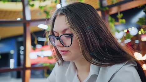 close up of young woman seated in bar, focusing intently in front of her with blurred background featuring vibrant colorful lights, evoking casual and contemplative mood