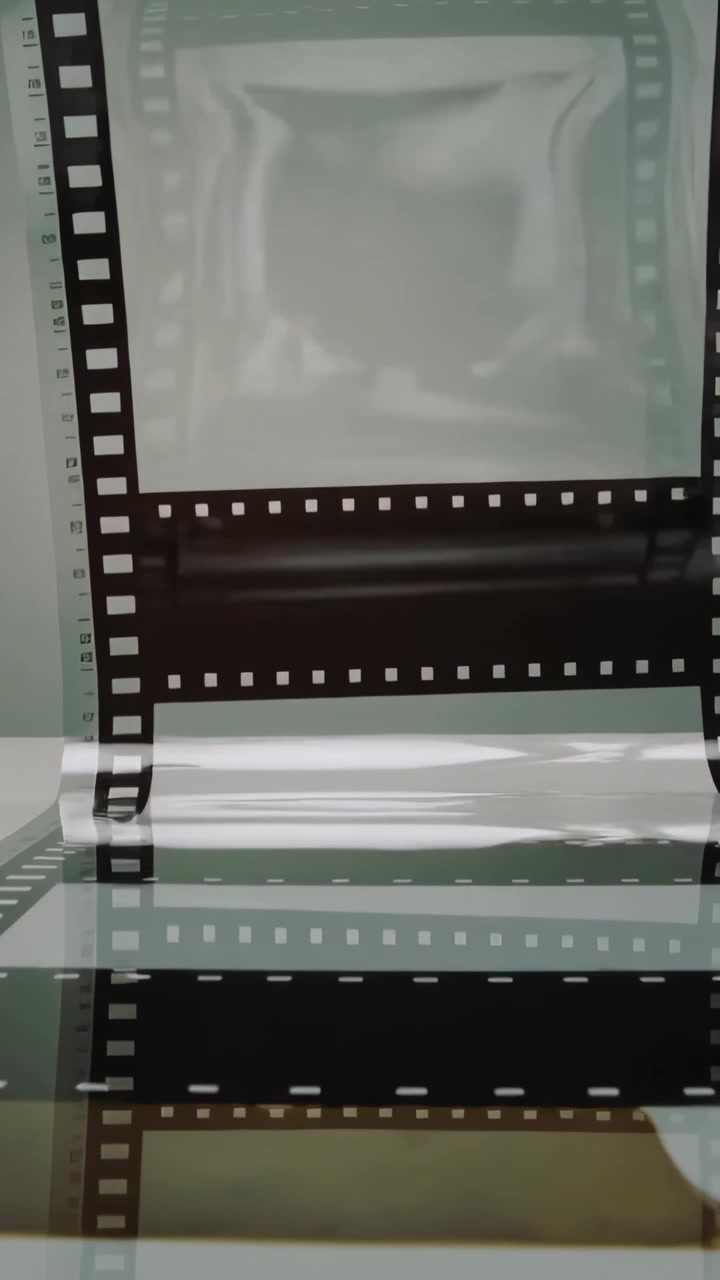 Video verticale: Striscia di pellicola che si srotola, tirata da mani invisibili su vetro per la scansione con un righello.