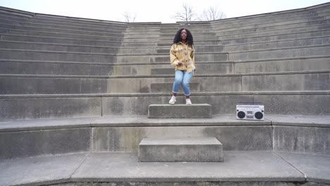 Smiling-black-woman-dancing-on-steps-in-park