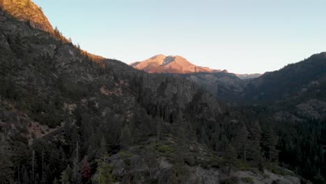 Panorámica-Aérea-De-Un-Camino-Ventoso-A-Través-Del-Paso-De-Sonora-En-California-Al-Atardecer-Con-árboles-En-Primer-Plano