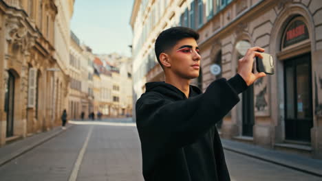 young person with bold makeup filming on smartphone in european city street