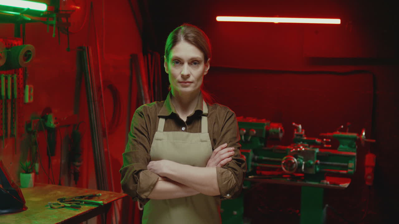 портрет молодой женщины в фартуке, смотрящей на камеру с серьезным лицом в металлической мастерской