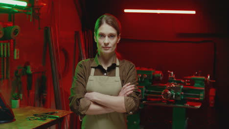 Portrait-of-young-woman-in-apron-looking-at-camera-with-serious-face-in-metal-workshop