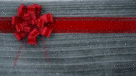 Animation-of-snow-falling-against-christmas-present-ribbon-on-wood