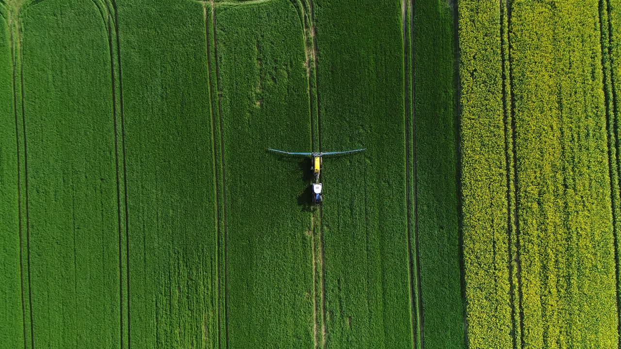 tractor con remolque y brazo metálico ancho con boquillas rociando pesticidas sobre el campo verde