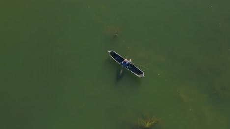 fisherman in traditional wooden canoe checking net and taking out fish, top down