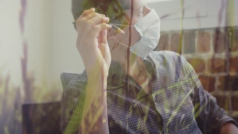 tall grass moving in the wind against caucasian man wearing face mask holding pen at office