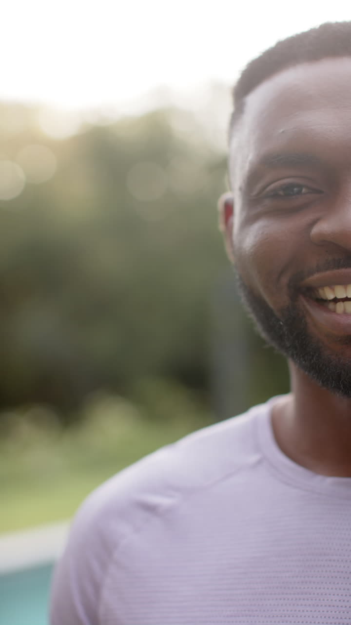 Vertical video portrait of happy african american man smiling in garden, copy space, in slow motion