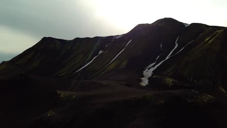 Aerial-landscape-view-of-Icelandic-highlands-dark-mountains,-with-small-patches-of-melting-snow,-on-a-cloudy-day