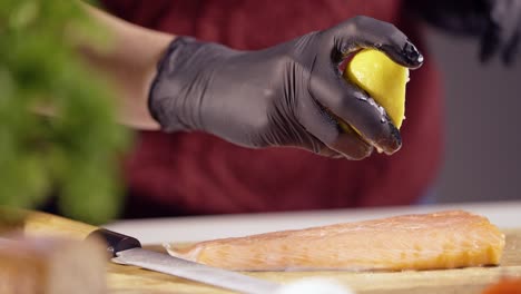 gloved hands squeezing fresh lemon juice over a salmon fillet. the droplets enhance the fish’s natural flavor, creating a gourmet touch. a sharp knife and fresh ingredients complete the food