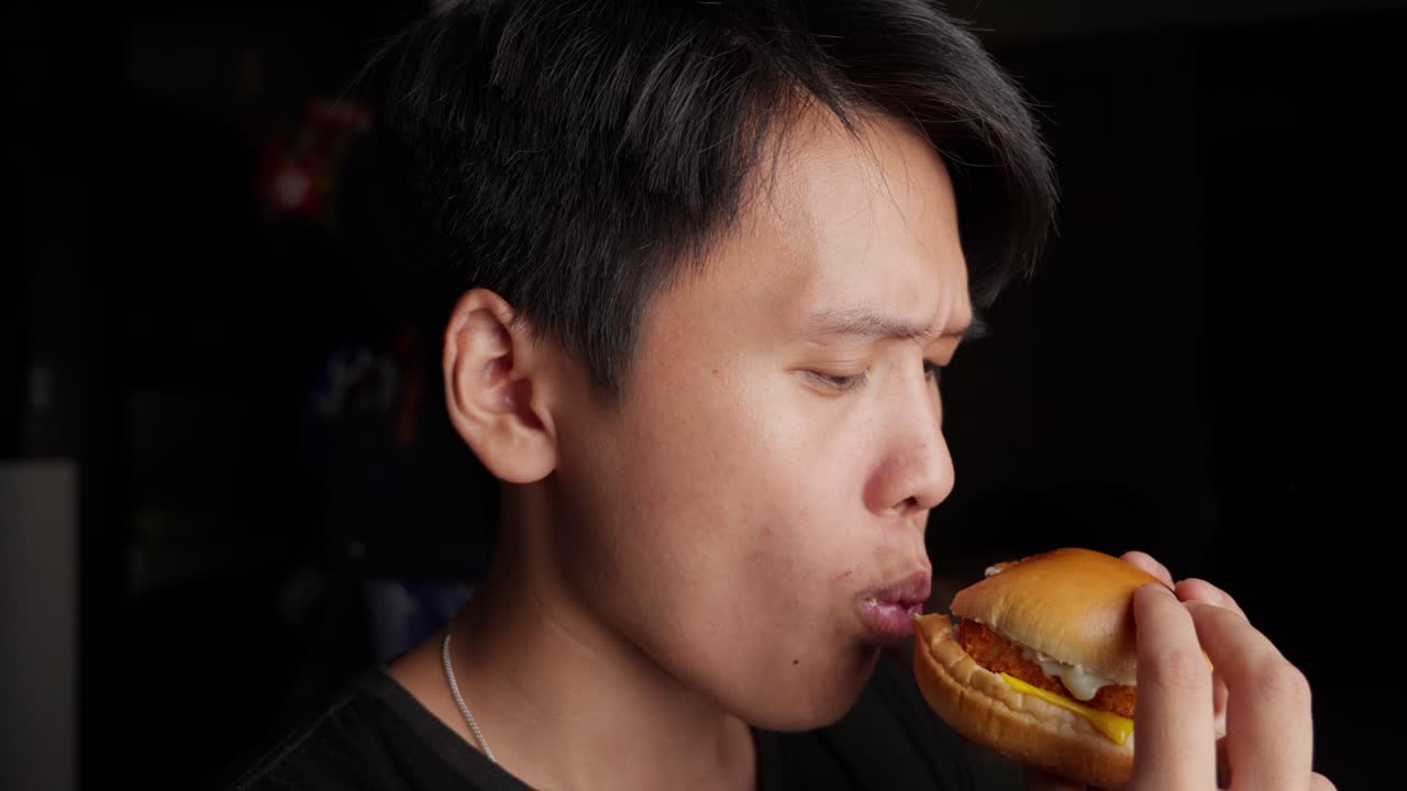 Young man enjoying a bite of a delicious fish sandwich with mayo and cheese