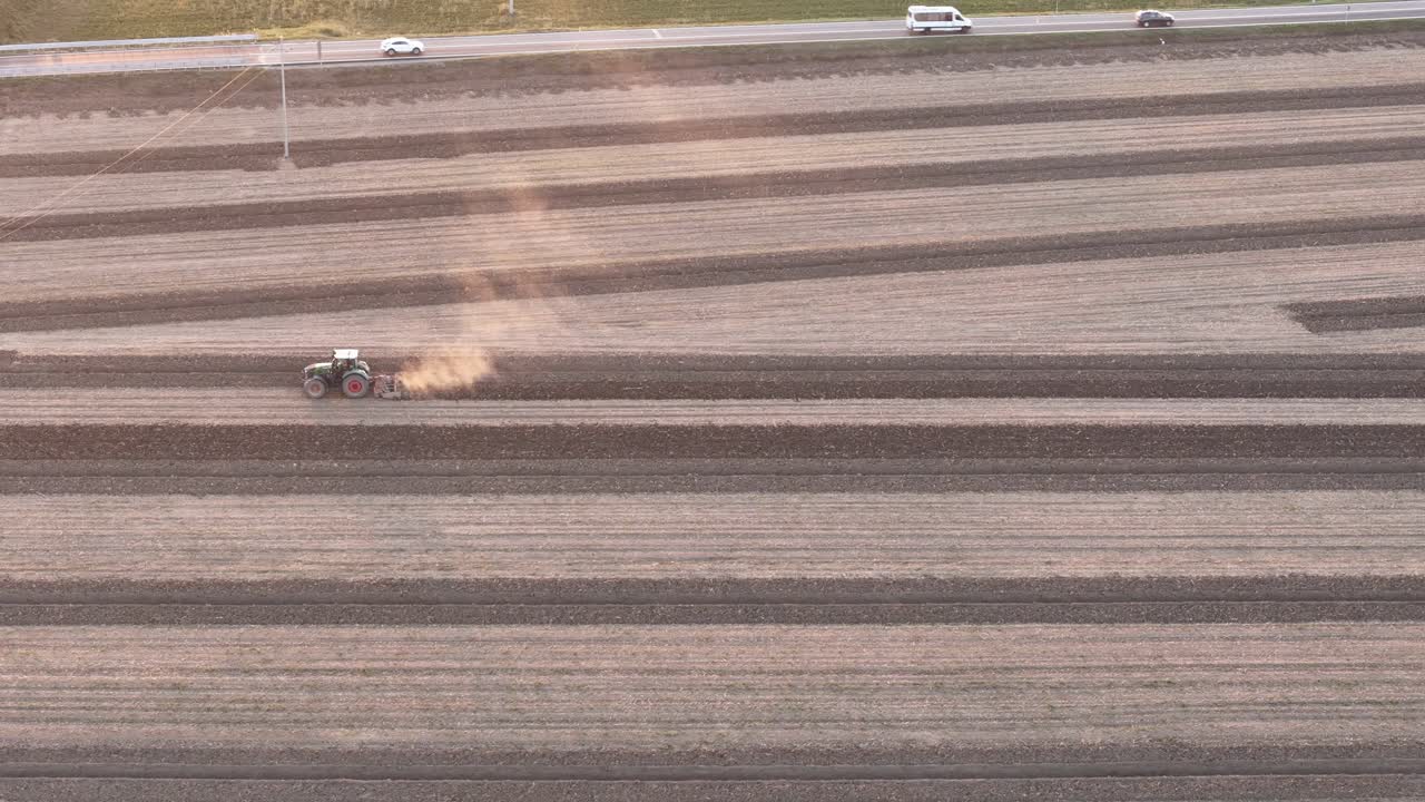 Tractor conducting deep tillage across structured rows in a dry Po Valley field, with visible dust plume and access road, near San Pietro al Cerro, PC, Italy