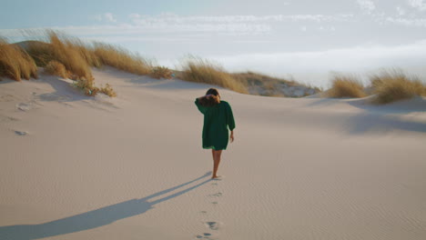 woman walking desert dunes in black dress. girl stepping sand making footmarks.