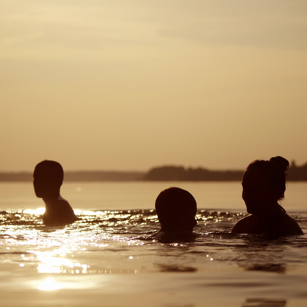 Mother throws up her sons into water at sunset. Silhouette of a woman and two children having fun together in the river in the evening.