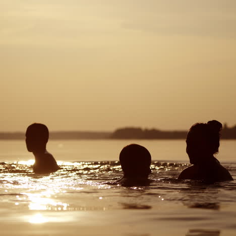 mother throws up her sons into water at sunset. silhouette of a woman and two children having fun together in the river in the evening.