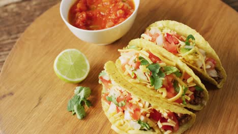 video of freshly prepared tacos and bowl with sauce lying on board on wooden surface