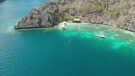 aerial drone shot over people swimming, between paraw boats in beautiful, shallow, clear, blue water, at coron island, in philippines, asia