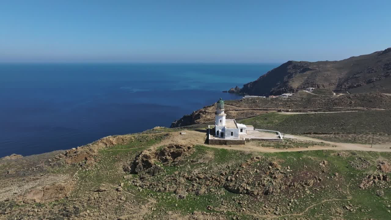 Orbiting the stunning landscape of Mykonos, with a lighthouse standing at the edge of the cape against the blue Aegean Sea