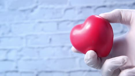 una mano en un guante médico sosteniendo un corazón rojo