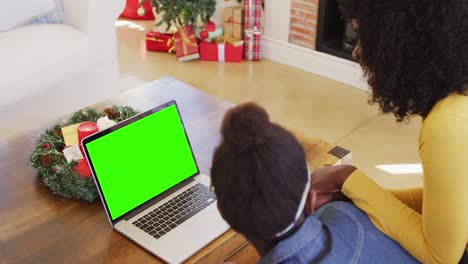 African-american-mother-and-daughter-using-laptop-with-green-screen-at-home