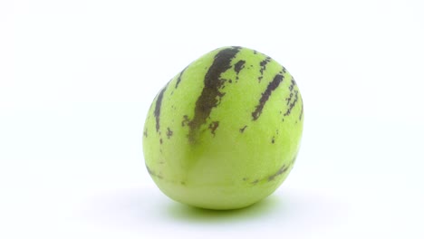 one whole green pepino is rotating on the turntable. water drops appears on the skin during rotation. isolated on the white background. close-up. macro.