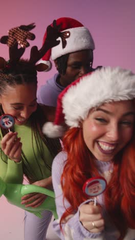 Vertical-Video-Studio-Shot-Of-Gen-Z-Friends-Dancing-And-Posing-For-Selfie-At-Christmas-Party-Wearing-Santa-Hat-And-Reindeer-Antlers-2