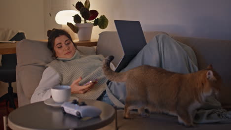 chilling brunette lying sofa watching laptop at evening room. woman resting