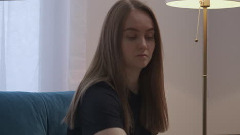 female-student-is-resting-at-home-alone-at-weekend-sitting-on-coach-opening-book-and-turning-on-floor-lamp-medium-portrait-of-reading-woman-indoors-calm-entertainment-at-evening