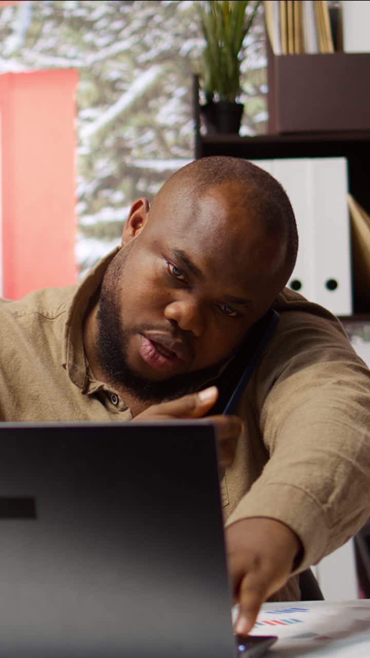 Afroamerikansk mand multitasker med bærbar computer og telefonopkald på kontor