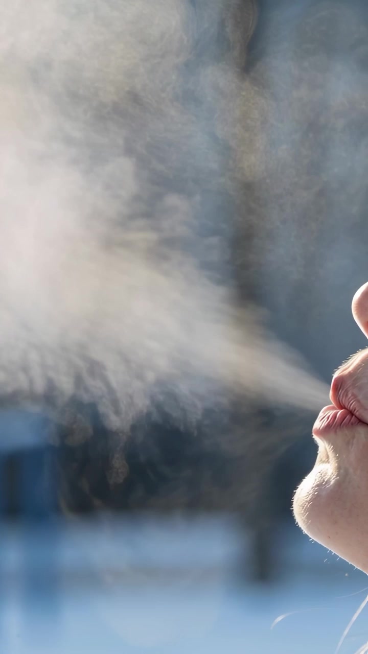 Vertical video: Exhaling woman in cold, pursing lips and blowing breath vapor in park, copy space