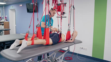 young therapist is training his client with special ropes in a modern rehabilitation center. professional trainer works with the patient with a suspension rope system indoors.