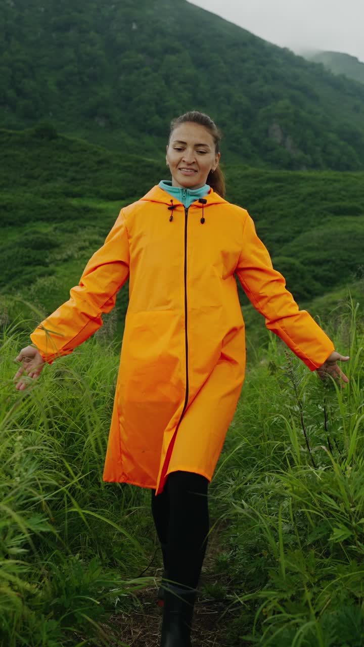 Happy Woman in Orange Raincoat Standing in Green Mountain Landscape
