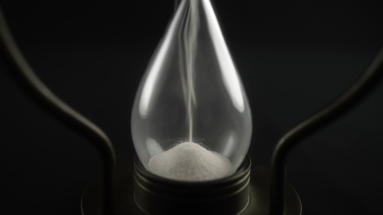 Close-up of White Sand Falling Through a Glass Hourglass