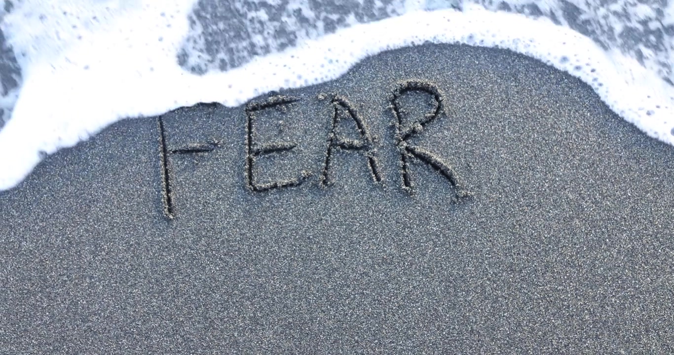 Soft white seafoam gently washes over sand with word fear