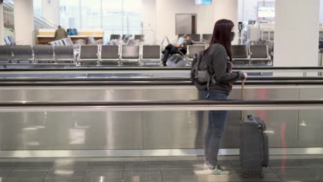 side shot of a young woman wearing mask rideing moving walkway with suitcase