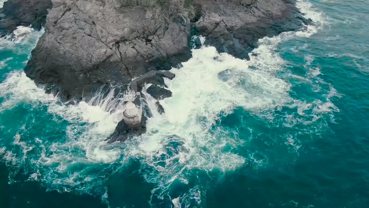 video de drone aéreo giratorio de agua de mar del océano azul y verde golpeando la costa donde están presentes acantilados escarpados y rocas